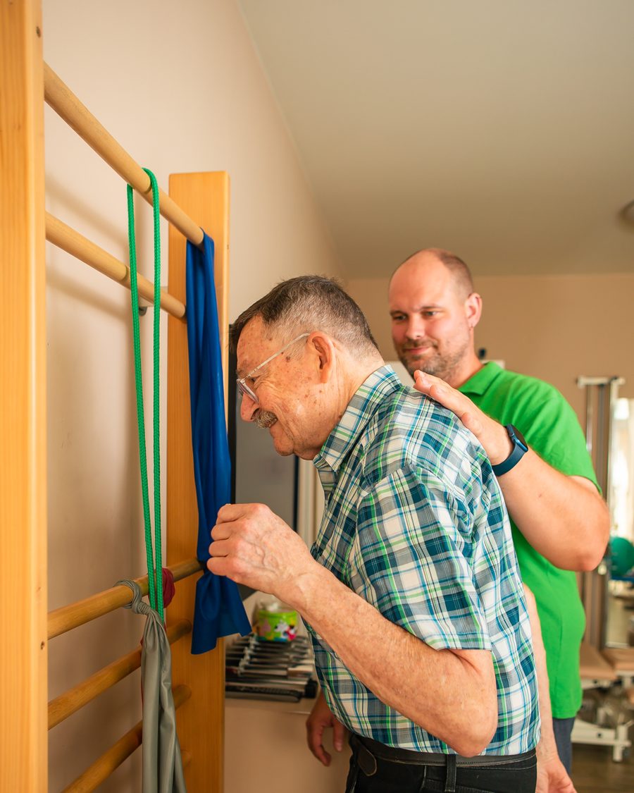 Patient trainiert an der Sprossenwand, begleitet von seinem Therapeuten