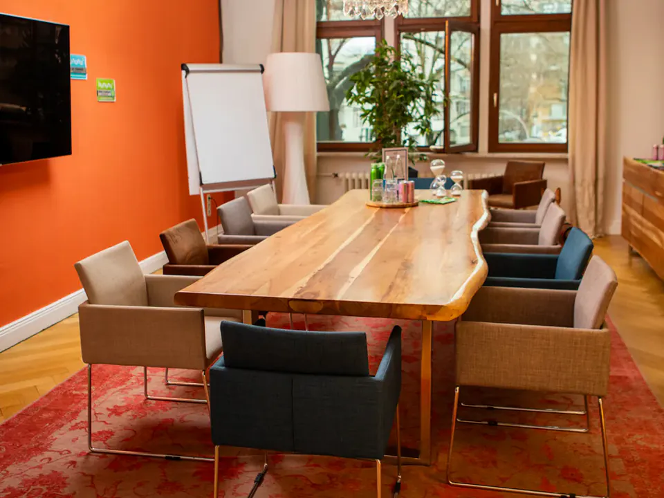 Heller Seminarraum mit langem Holztisch und Flipchart