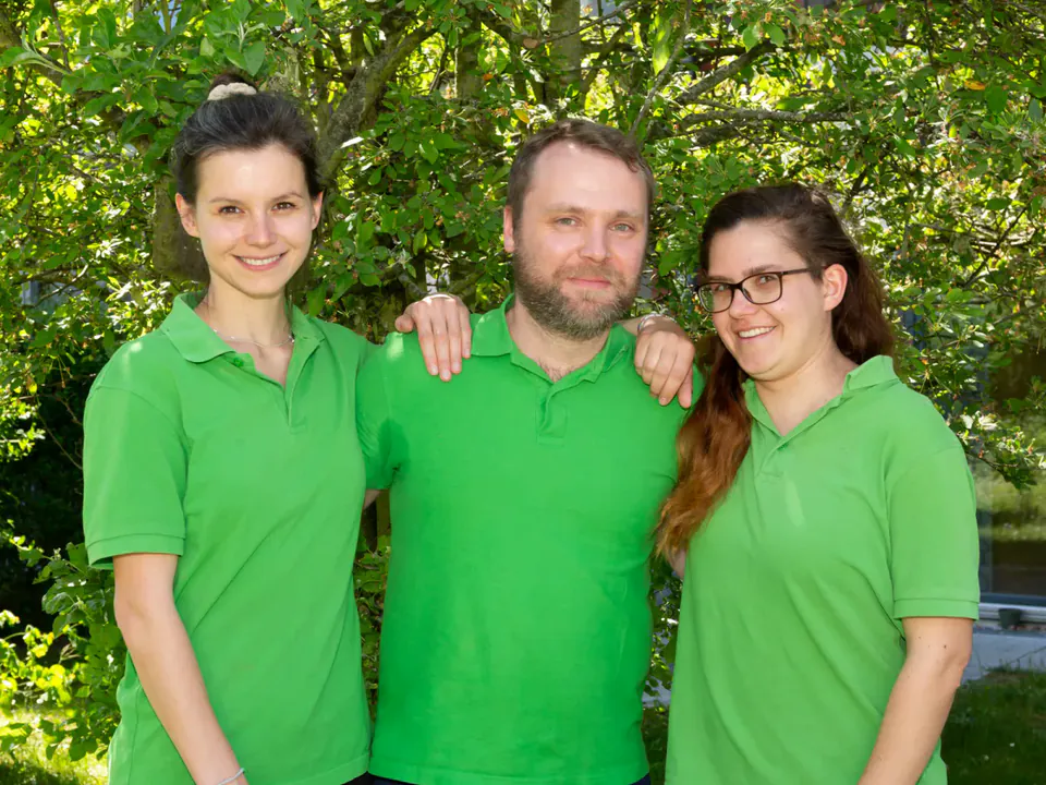 Drei aus dem Team in grünen Poloshirts lächeln im Grünen