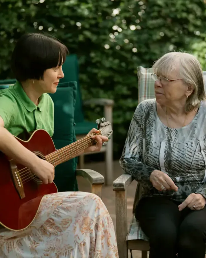 Therapeutin spielt im Garten Gitarre für eine Bewohnerin